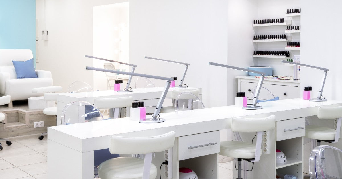 A modern-looking, clean nail salon with all-white stations and pedicure chairs. The back wall is painted light blue.